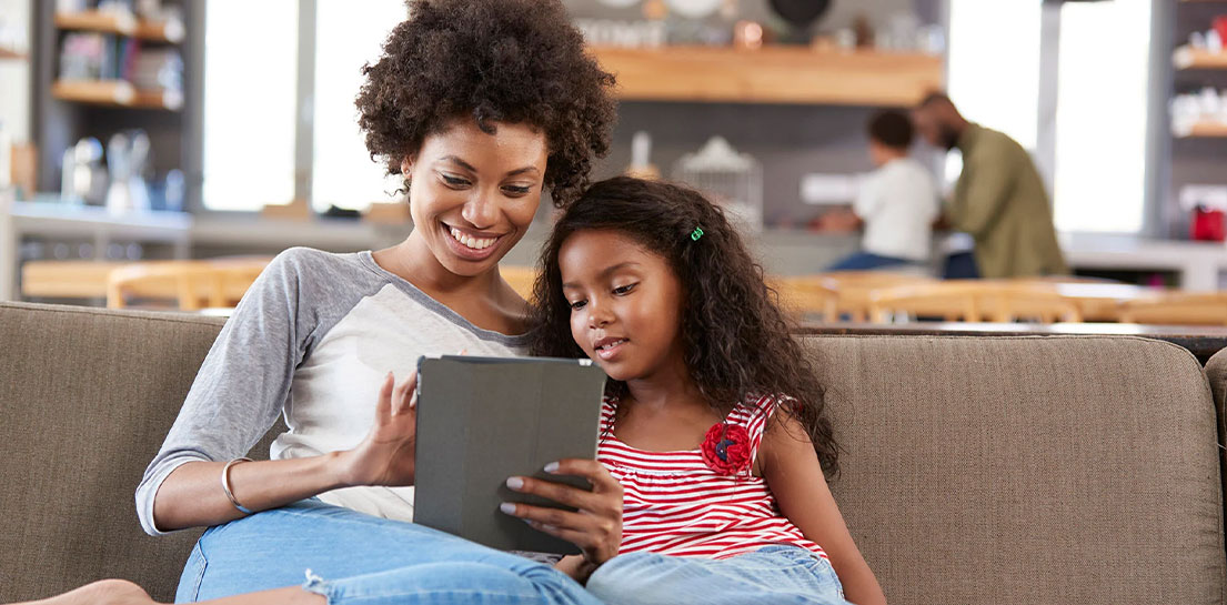Mother and young daughter sitting on sofa with tablet during a virtual doctor&rsquo;s visit with video