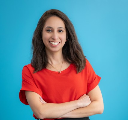 Smiling woman in red shirt with arms crossed against a blue background