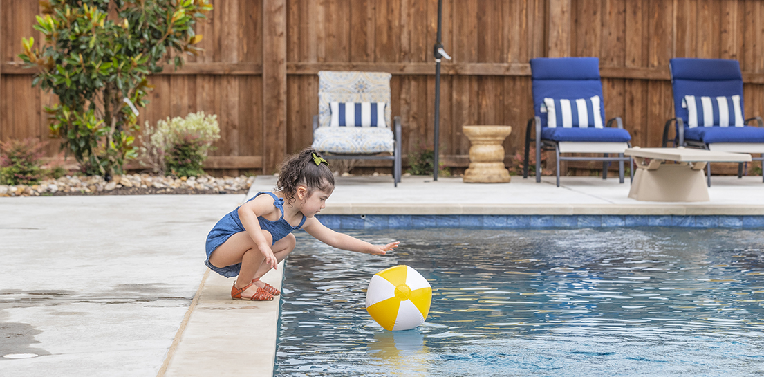 Child reaching for ball over a pool