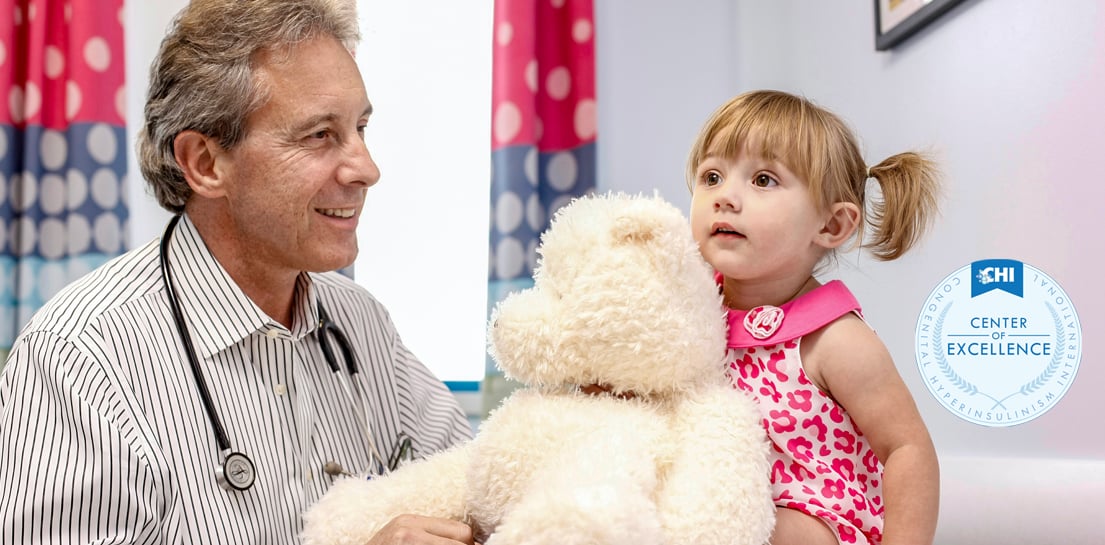 Doctor Paul Thornton and toddler patient in pink dress with white fluffy teddy bear