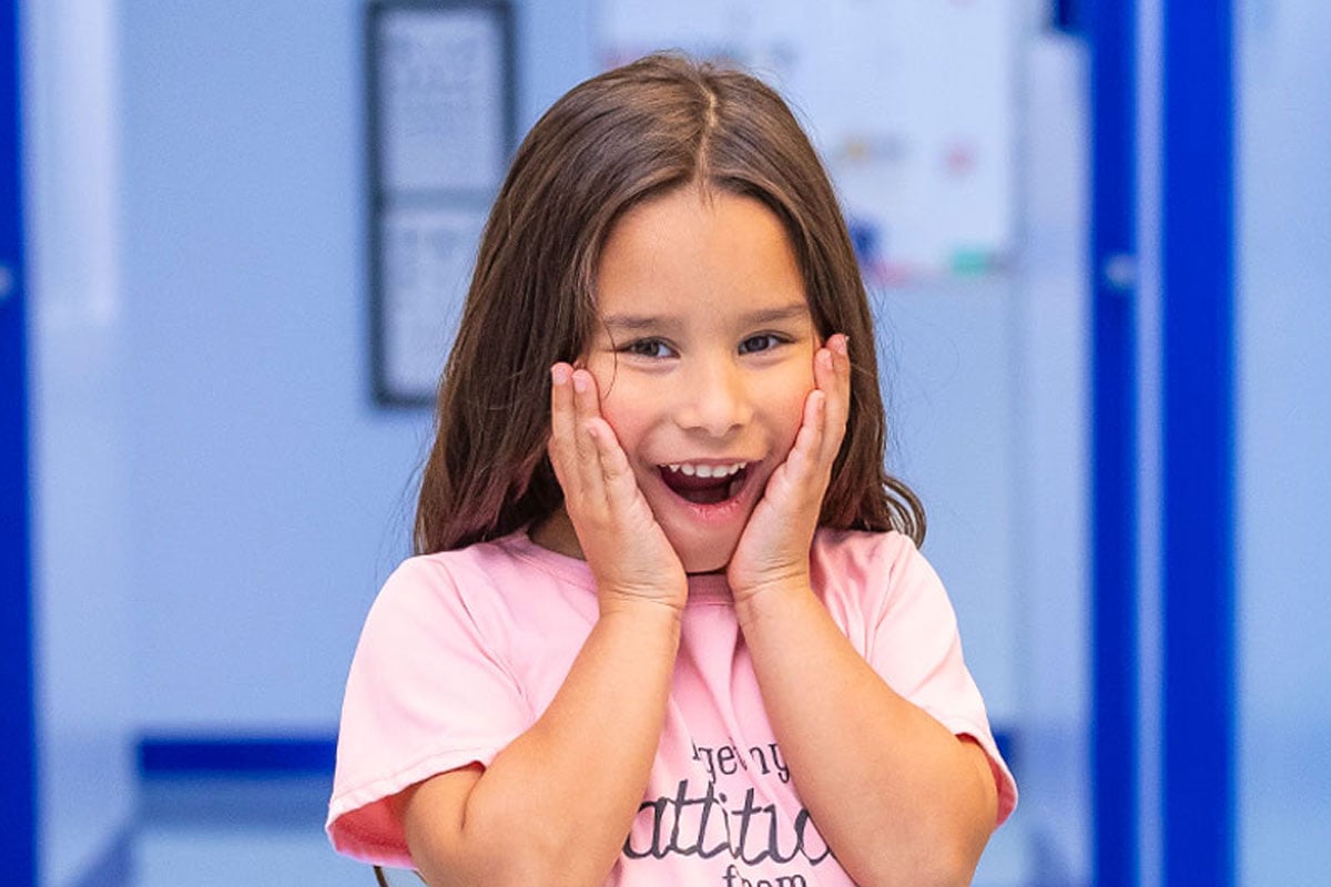 Young girl with excited smile with hands on face wearing a pink shirt