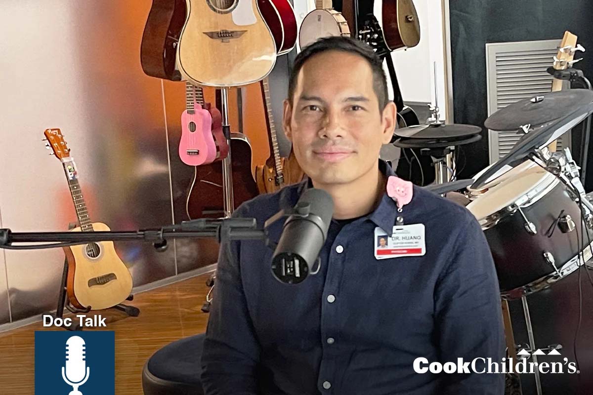 Dr. Huang speaking into a microphone with guitars and drums in the background. Logos: Doc Talk and CookChildren's