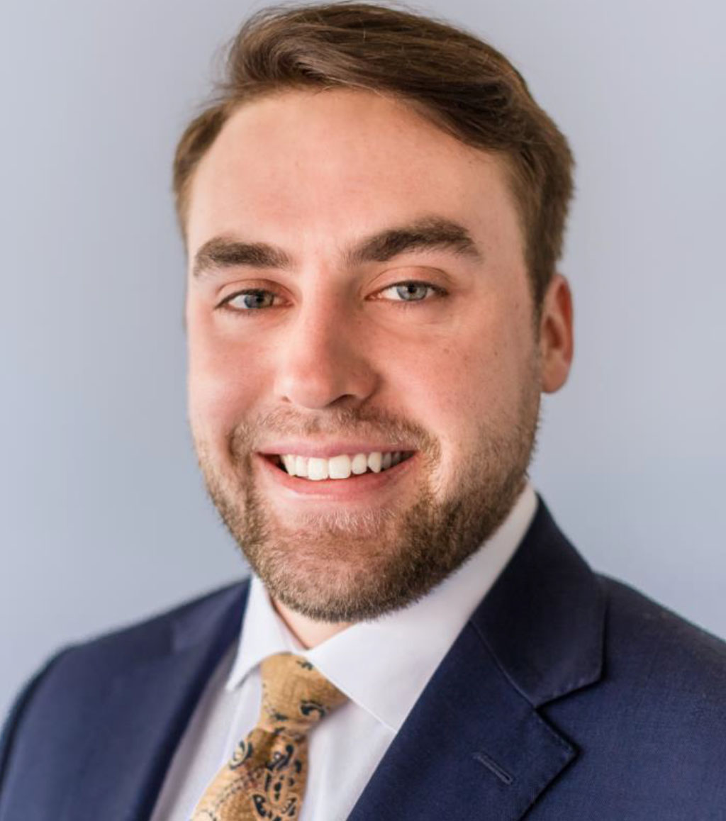 Smiling man in a dark blue suit, white shirt, and patterned gold tie