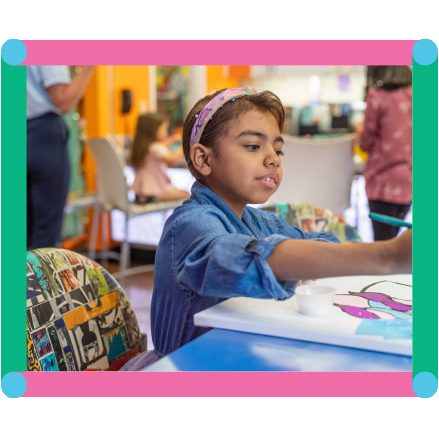 Young child painting with colorful paints on a canvas at a blue table