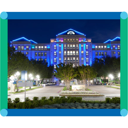 Cook Children's sign at the entrance of a large building, lit blue and purple at night