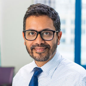 Smiling male professional in glasses, blue tie, and collared shirt