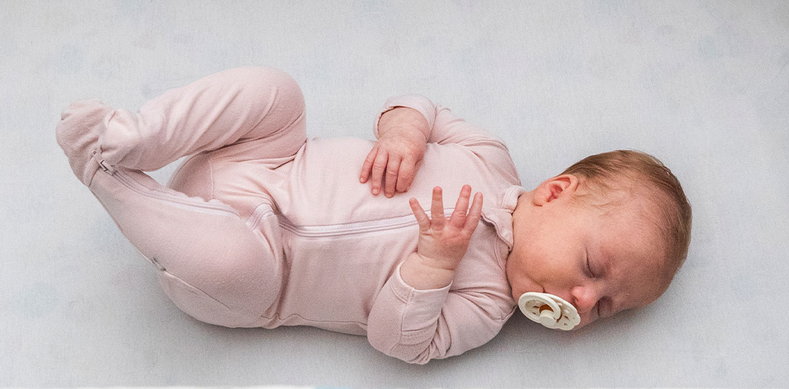 Sleeping baby with pacifier and wearing a pink sleep and play