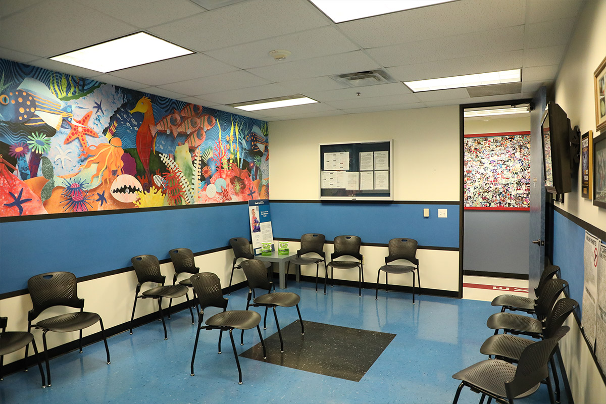 Vibrant children's waiting room with an underwater mural, blue and white walls, black chairs, and bright lights