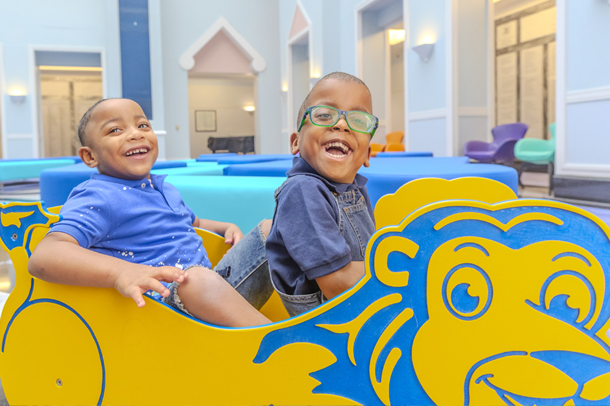 Two laughing boys playing in a yellow and blue lion-shaped toy
