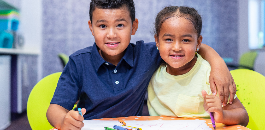 Two happy children coloring at a table; boy's arm around girl