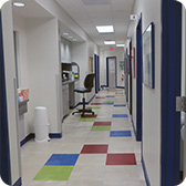 A long, bright clinic hallway with colorful square floor tiles, multiple doors, and a counter area with a sink and chair