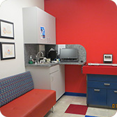 Red and white medical exam room with a red bench, sink, computer, and red exam table