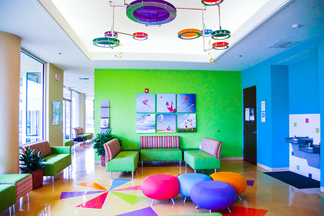 Vibrant children's waiting room with green and blue walls, colorful seating, kite art, and decorative ceiling lights