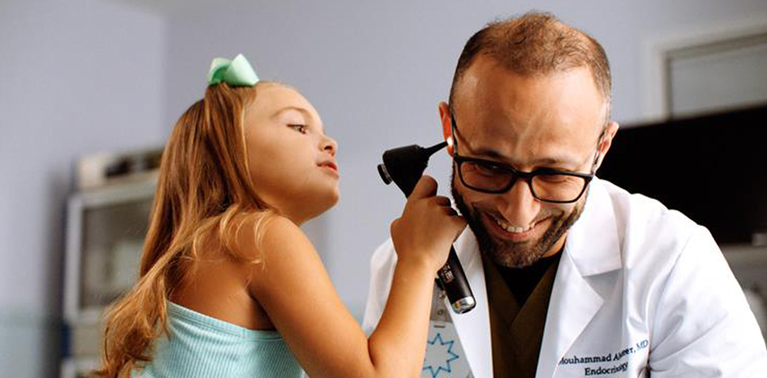 Young girl with a bow playfully uses an otoscope on smiling Dr. Mouhammad Amer, MD (Endocrinology)