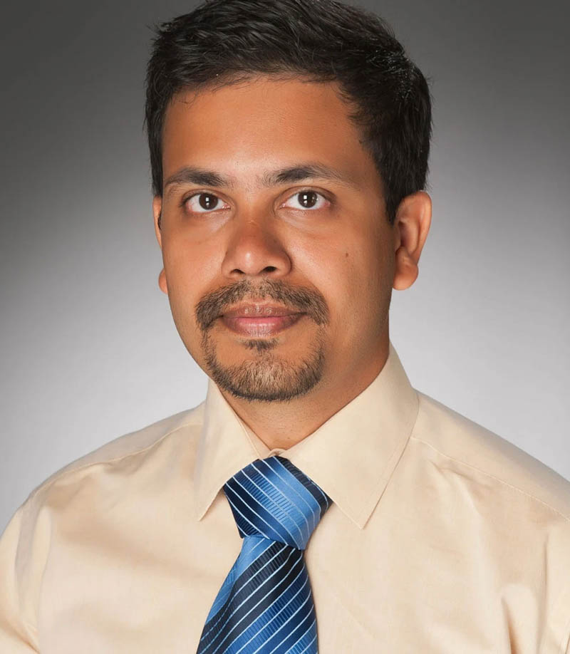 Man in beige shirt and blue striped tie, with dark hair and goatee, looking forward