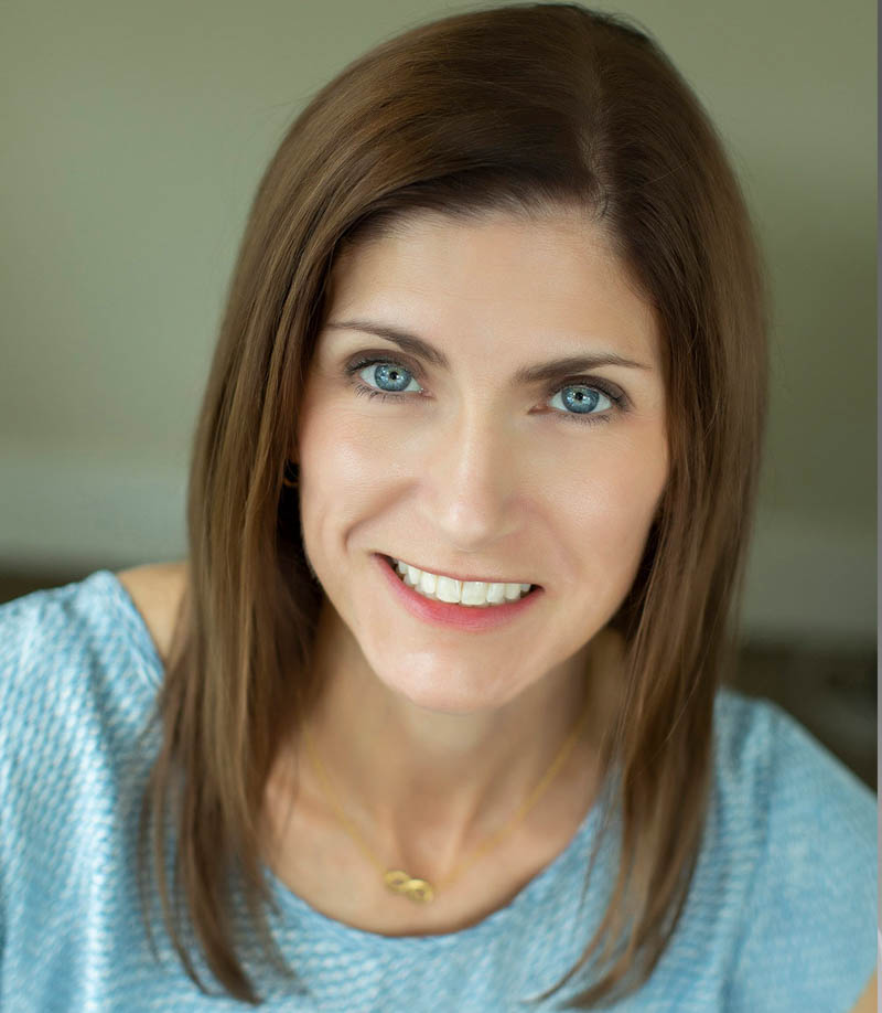 Smiling woman with blue eyes and brown hair wearing a light blue top