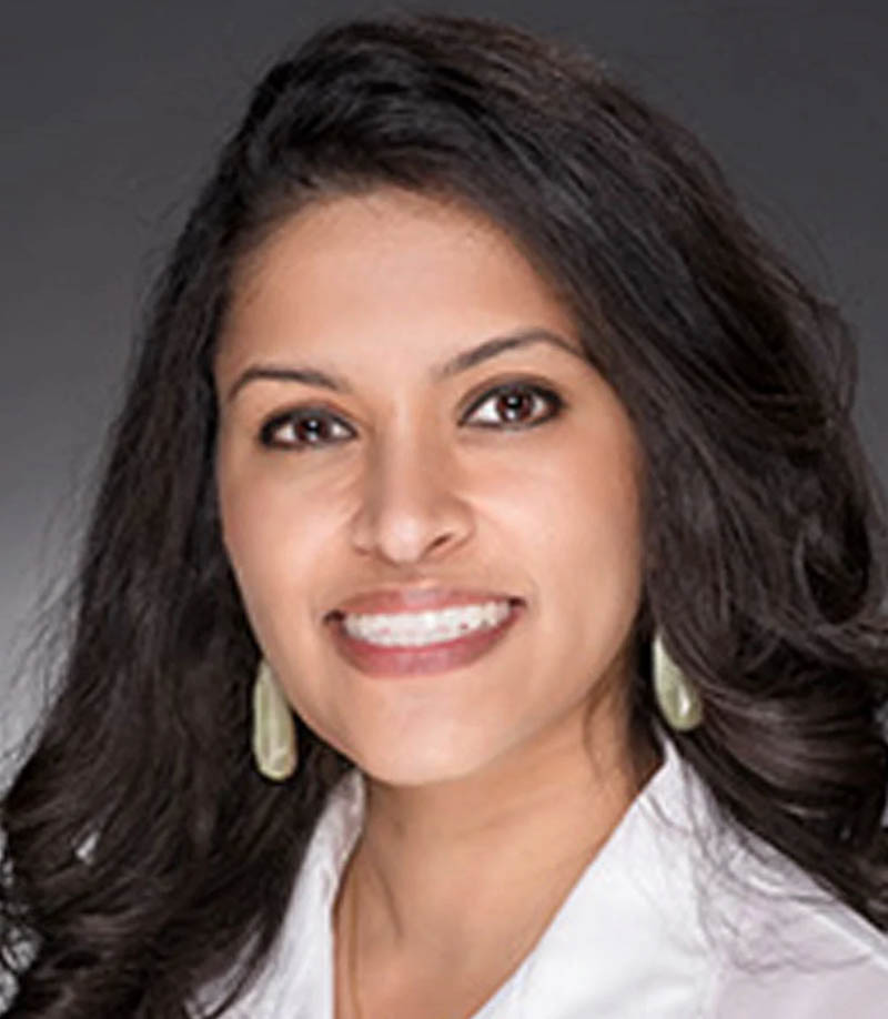 Professional headshot of a smiling woman with long dark hair and light teardrop earrings