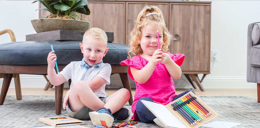Little blonde boy and girl sitting on floor with paper, pencils, and crayons