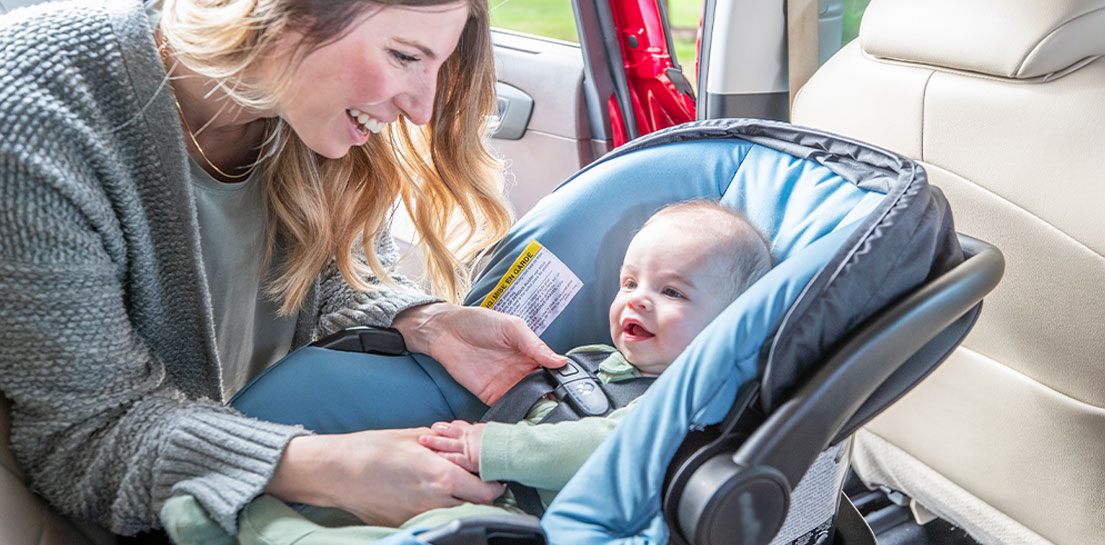 Mom putting baby in car seat and checking that harness is secure