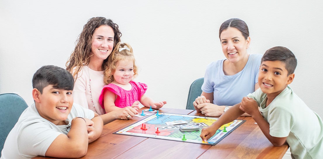 Two moms and 3 children playing a board game at the table