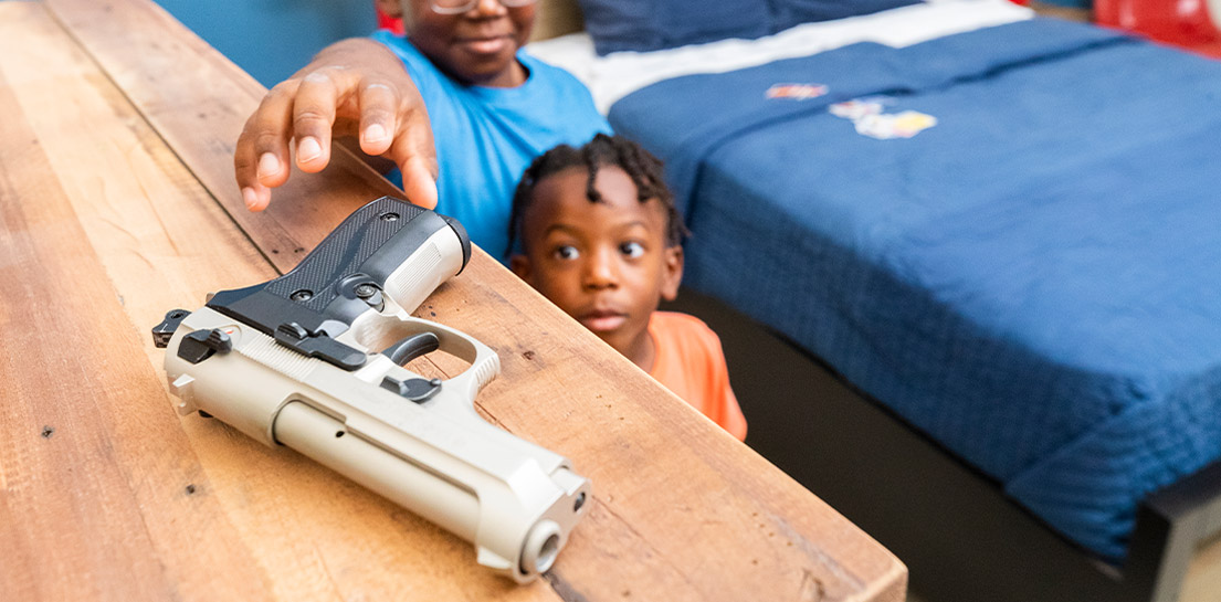 Two boys reaching for gun on dresser
