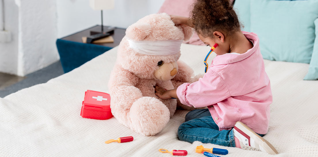 Little girl in pink top giving her teddy bear first aid with a first aid playset
