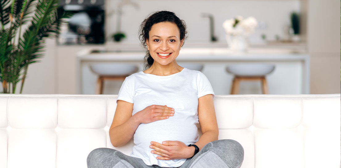 Pregnant woman with sitting on a sofa with her hands on her belly