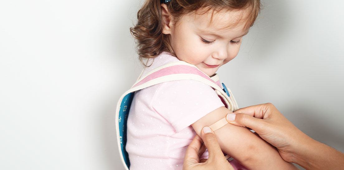 Little in pink shirt watching as a small bandage is put on her arm