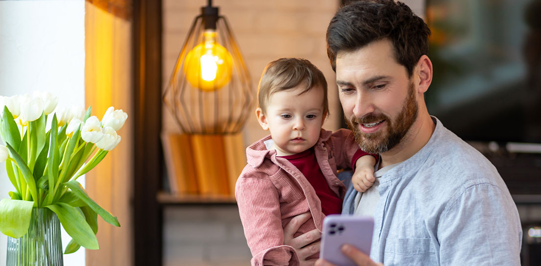 Father holding toddler son while sending a text to the pediatrician on the MyCookChildren&rsquo;s app