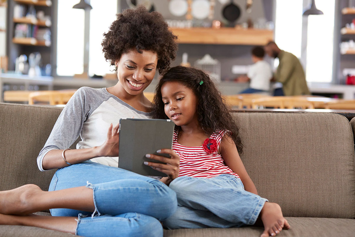 African-American mom and daughter on sofa and looking at a computer tablet