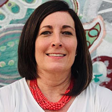 Headshot of a smiling professional woman with dark hair, white top, and red necklace