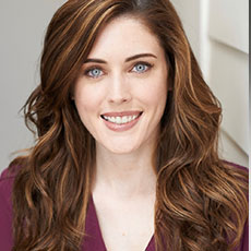 Professional headshot of a smiling woman with long brown hair and blue eyes