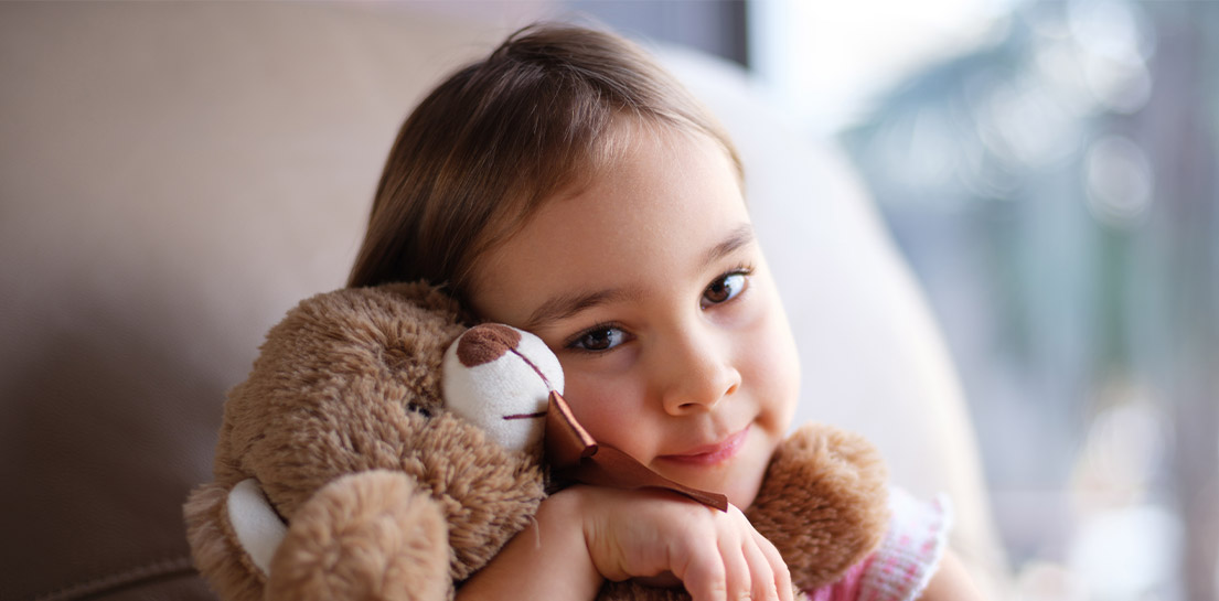 Smiling girl with dark eyes hugging a brown teddy bear