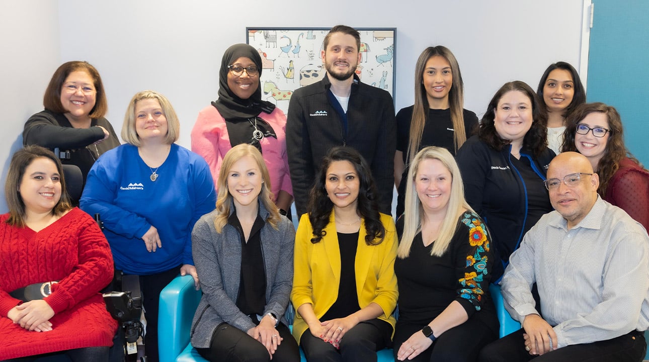Smiling diverse team of 12 professionals, two wear CookChildren's logo shirts. One person in a wheelchair