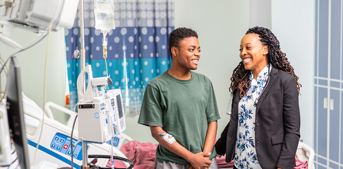 Young male patient with IV on arm and female doctor smiling at each other in hospital room