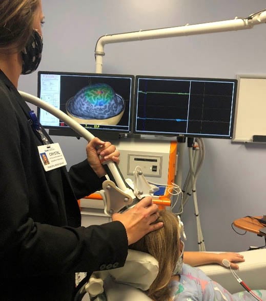 CRYSTAL operates a brain stimulation device on a child; monitors display a 3D brain model and data graphs