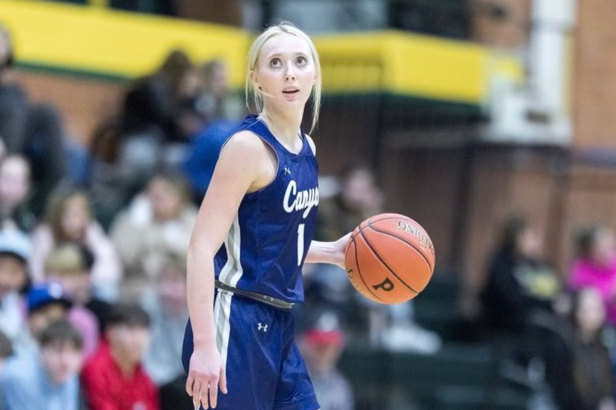 Blonde female basketball player in blue Canyon 1 jersey holds a Spalding basketball, looking up