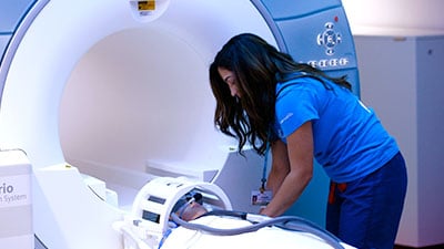 Healthcare worker helps patient into a Siemens Trio System MRI machine. Patient is prepped with a head coil
